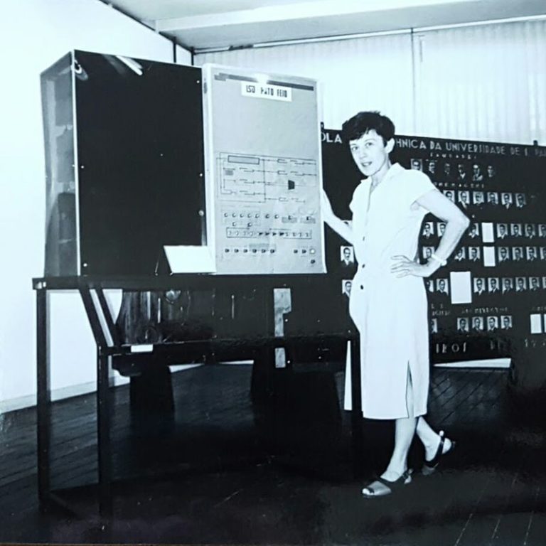 Foto em preto e branco de uma mulher ao lado do computador 'Patinho Feio' da USP, apontando para seu painel.